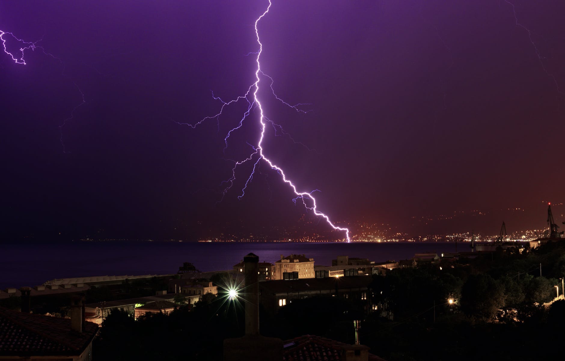 thunderbolt flashing in purple night sky over coastal town